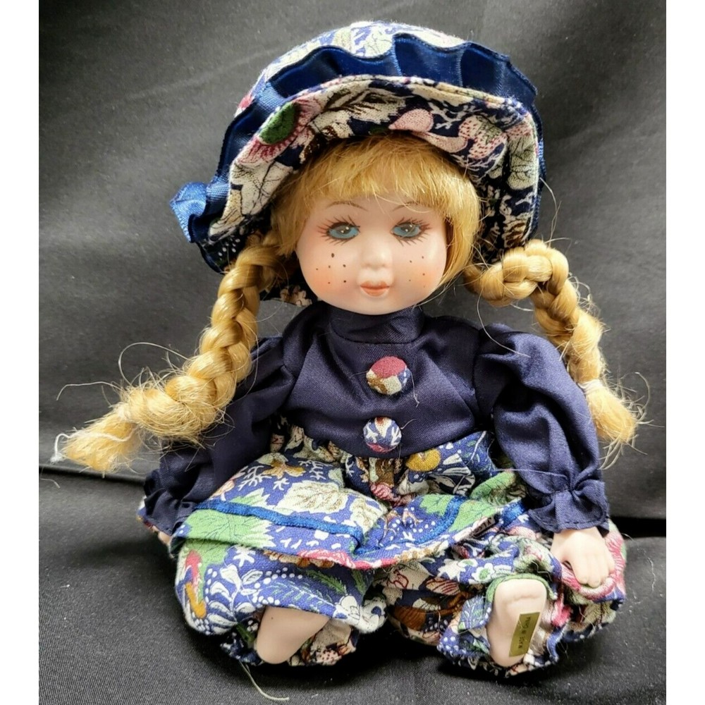 Porcelain Doll Sitting with Blonde Braids and Floral Bottoms and Hat
